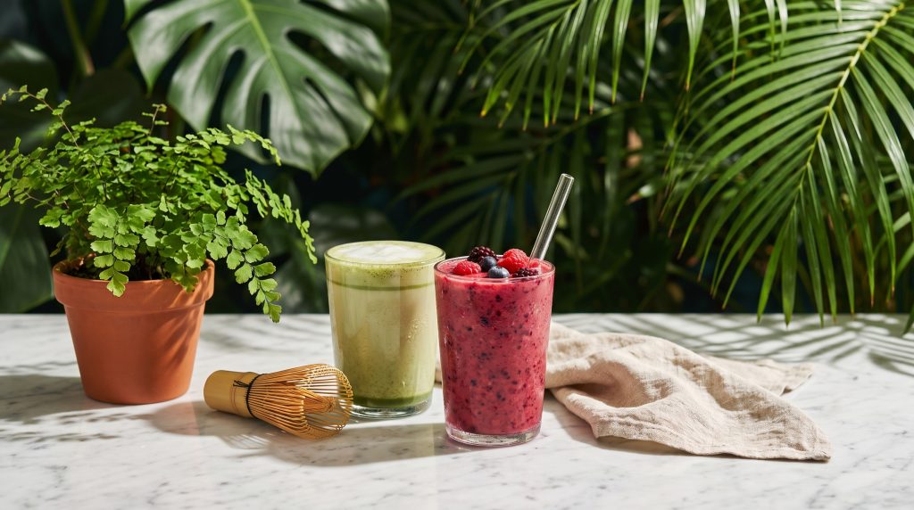 A matcha latte and a berry smoothie set down together on a marble table