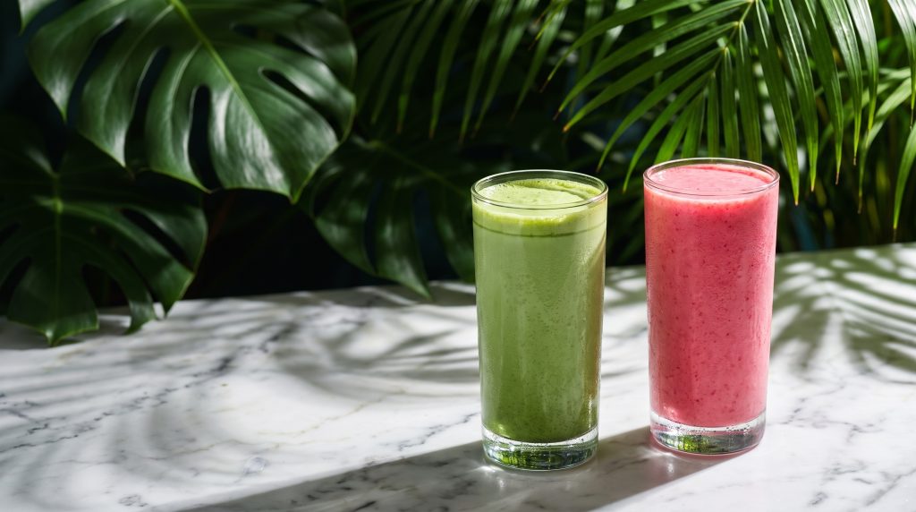A matcha latte and a pink smoothie lit dramatically on marble